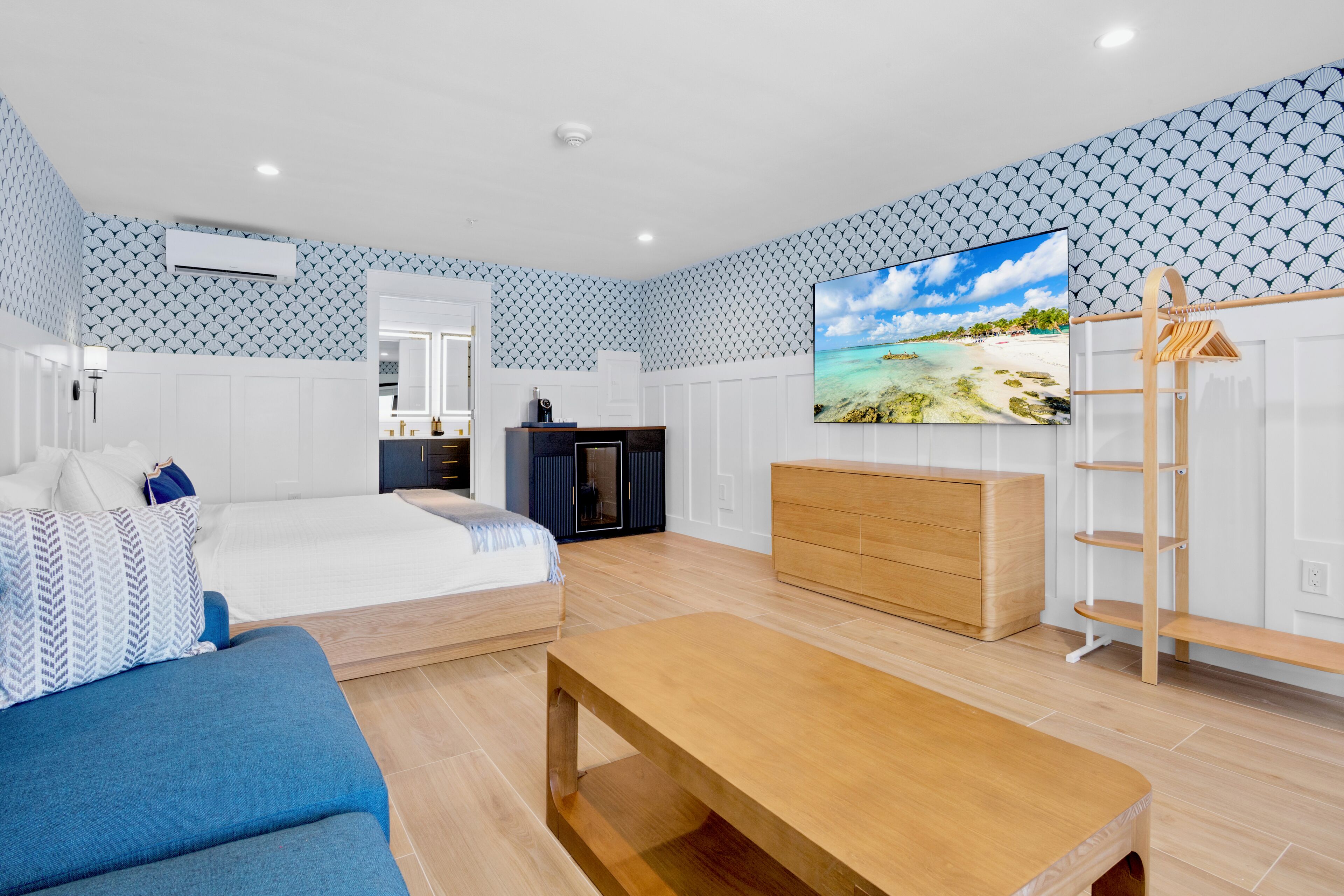 A modern bedroom with a bed, a wooden dresser, a TV, and a wooden bench.