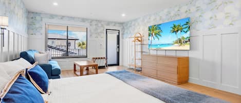 A bedroom with a bed, a sofa, a TV, a dresser, and a window with blinds.