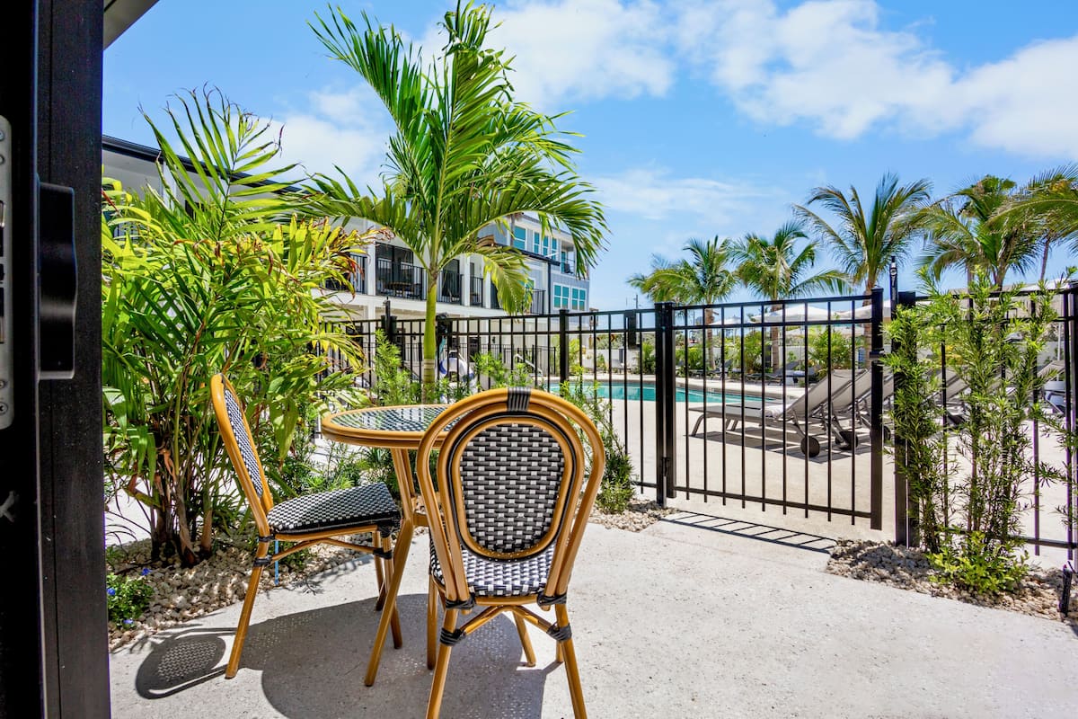 A patio with two wicker chairs and a table, overlooking a pool and a building with balconies.
