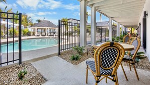 A covered outdoor area with a pool, lounge chairs, and a dining table with chairs.