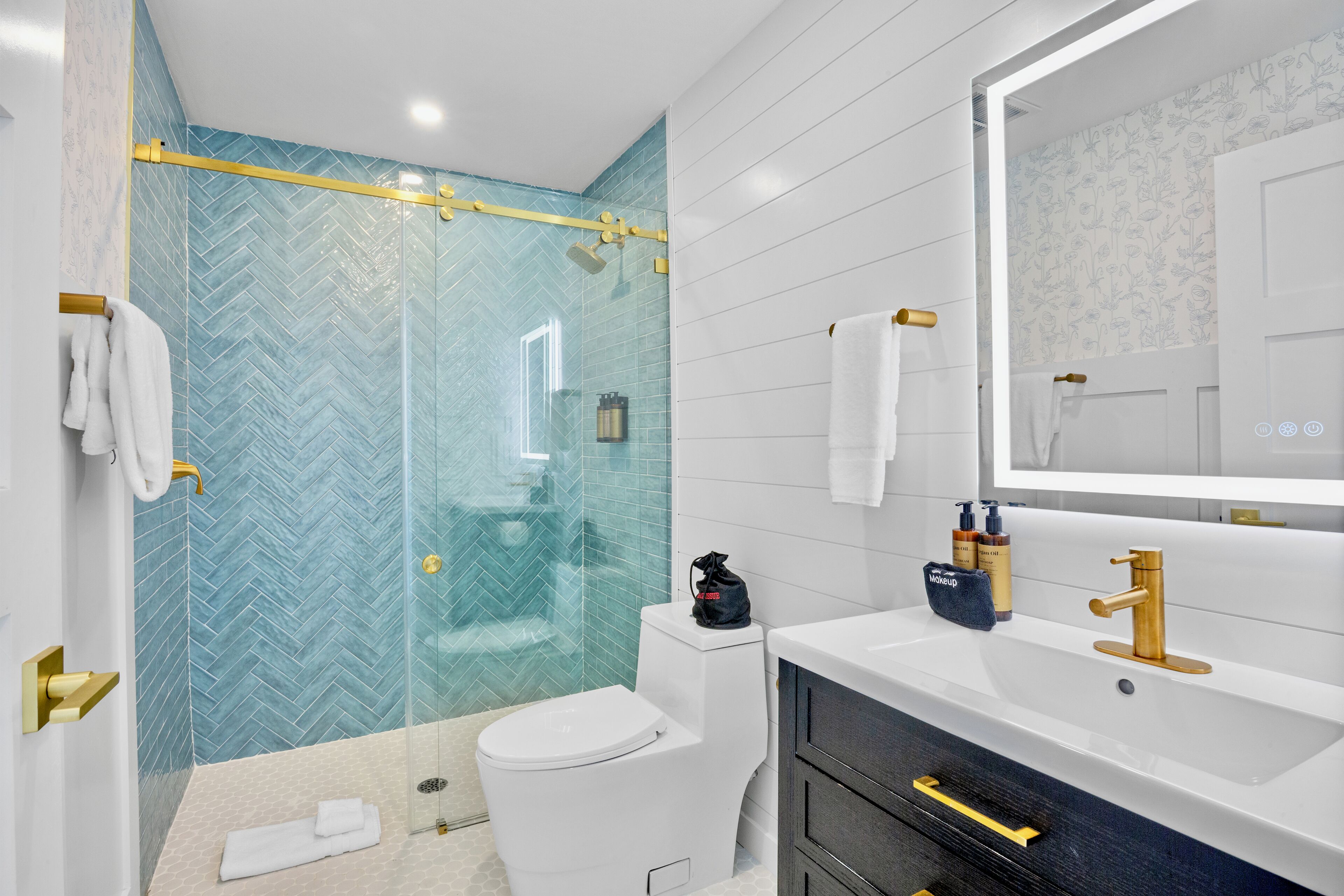 A modern bathroom with a glass shower enclosure, a white toilet, a vanity with a gold faucet, and a mirror.
