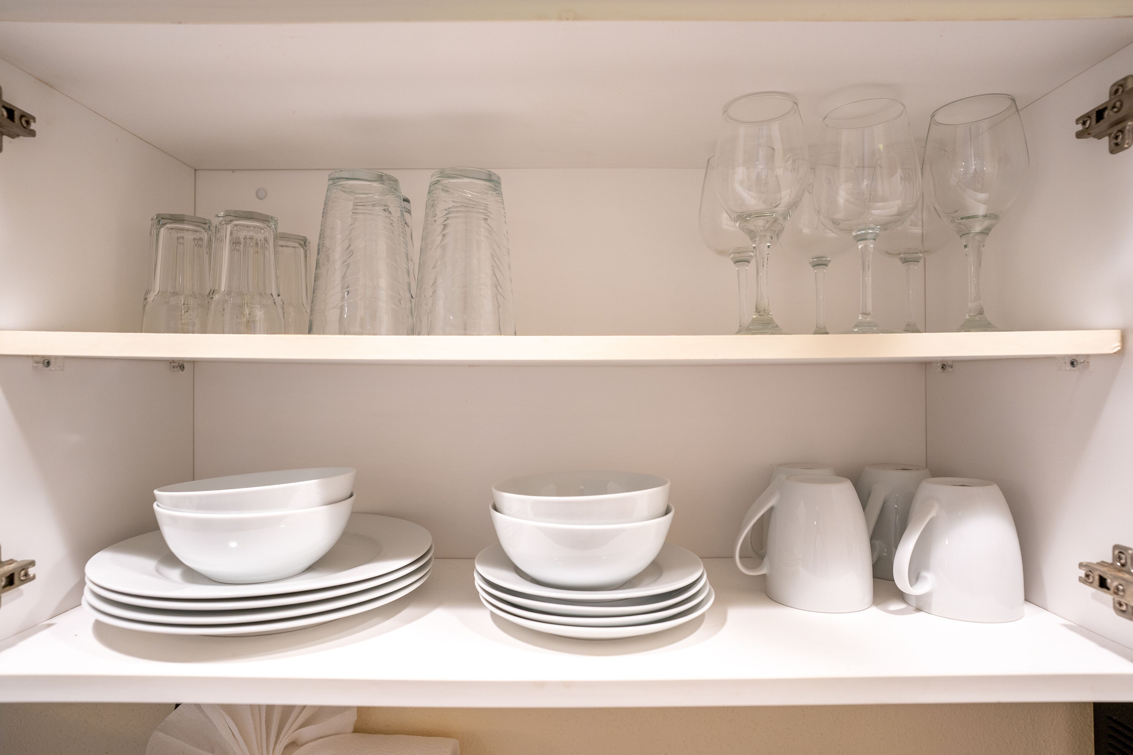 A white shelf with stacked white bowls, plates, and clear glassware.