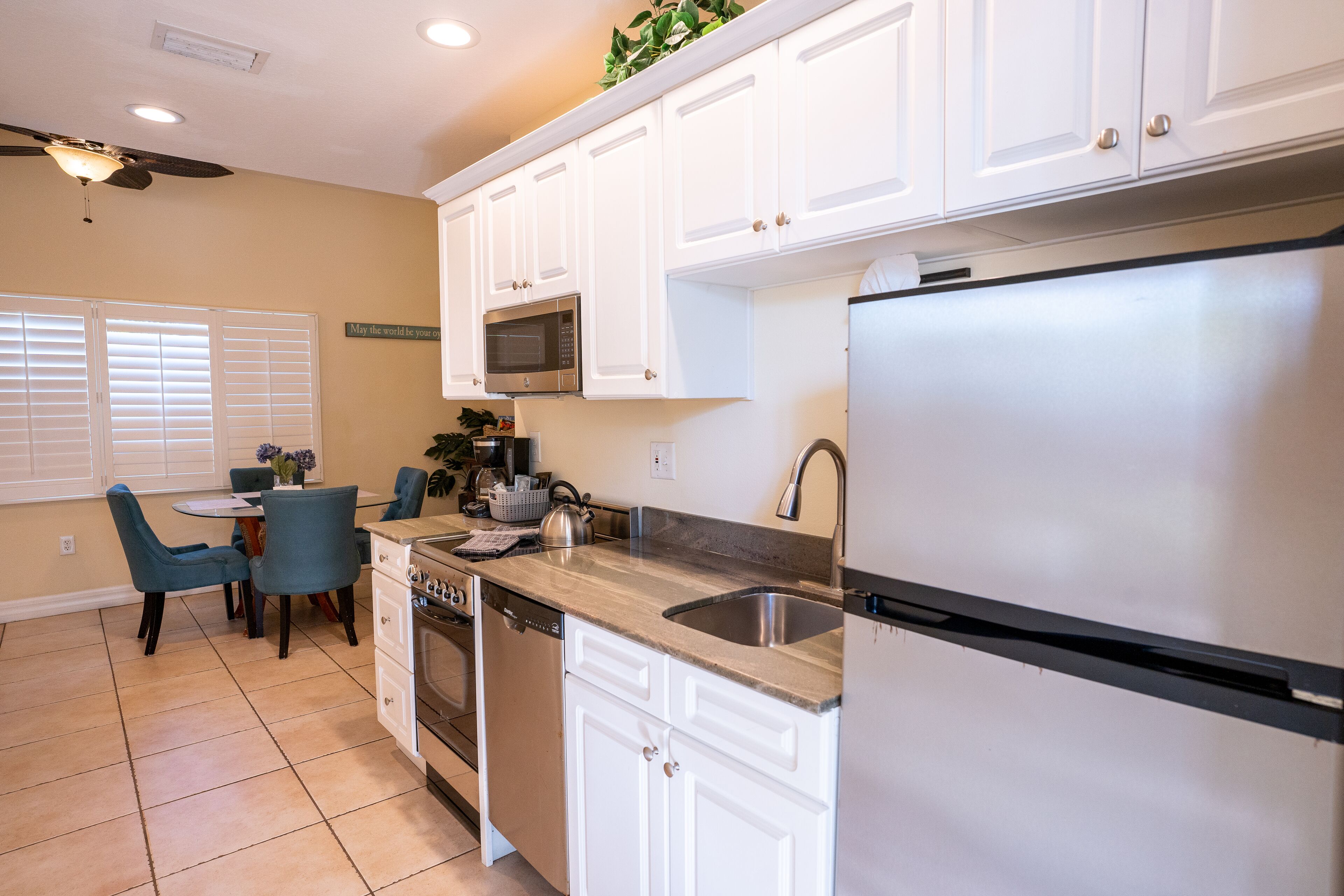 A kitchen with white cabinets, a stainless steel refrigerator, a microwave, and a dishwasher. There is a dining table with chairs and a ceiling fan.
