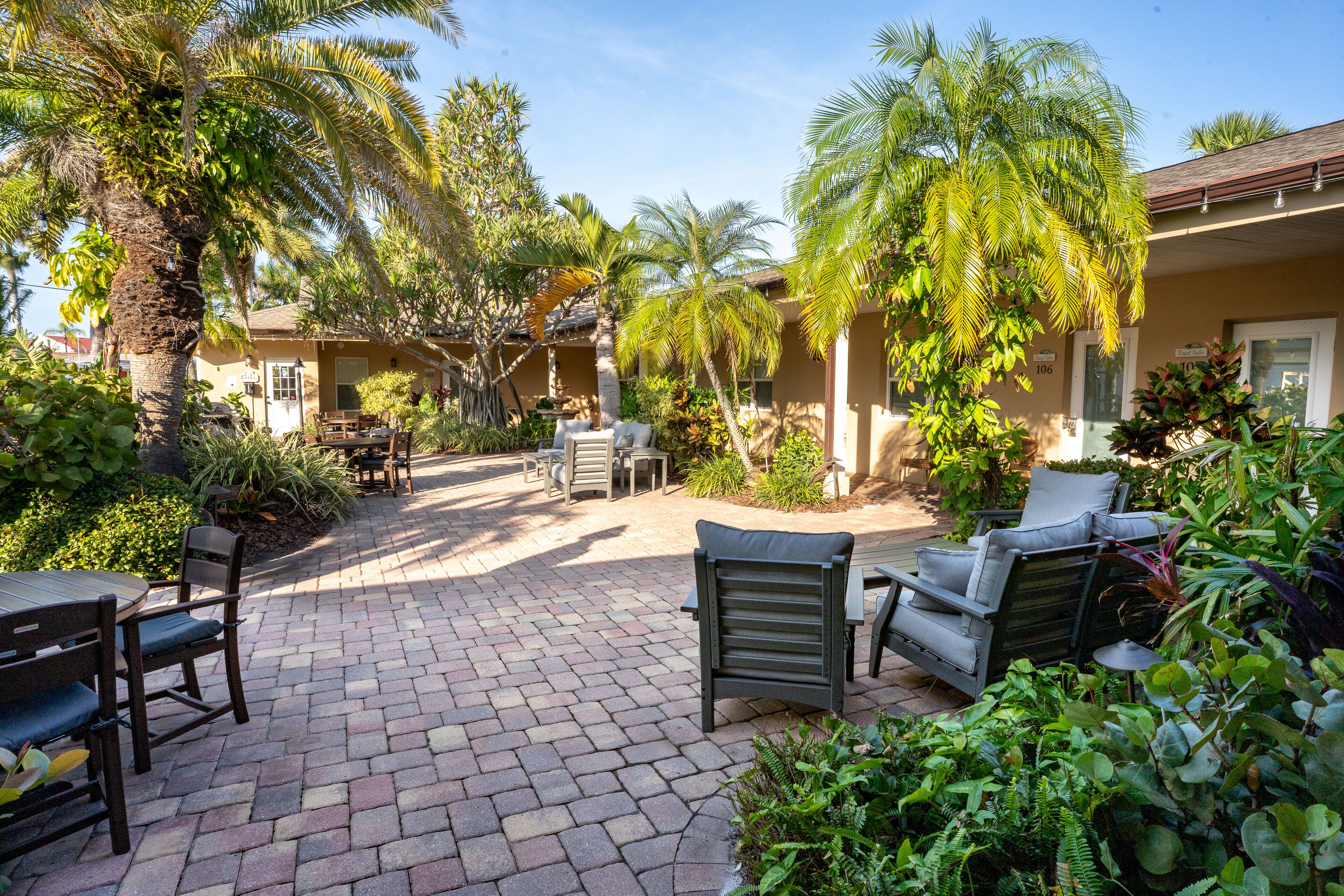 A patio area with outdoor seating, palm trees, and a brick pathway.