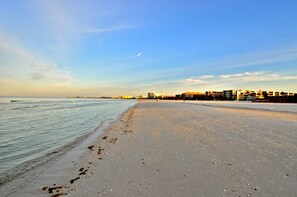 A wide beach with a clear sky and distant buildings.