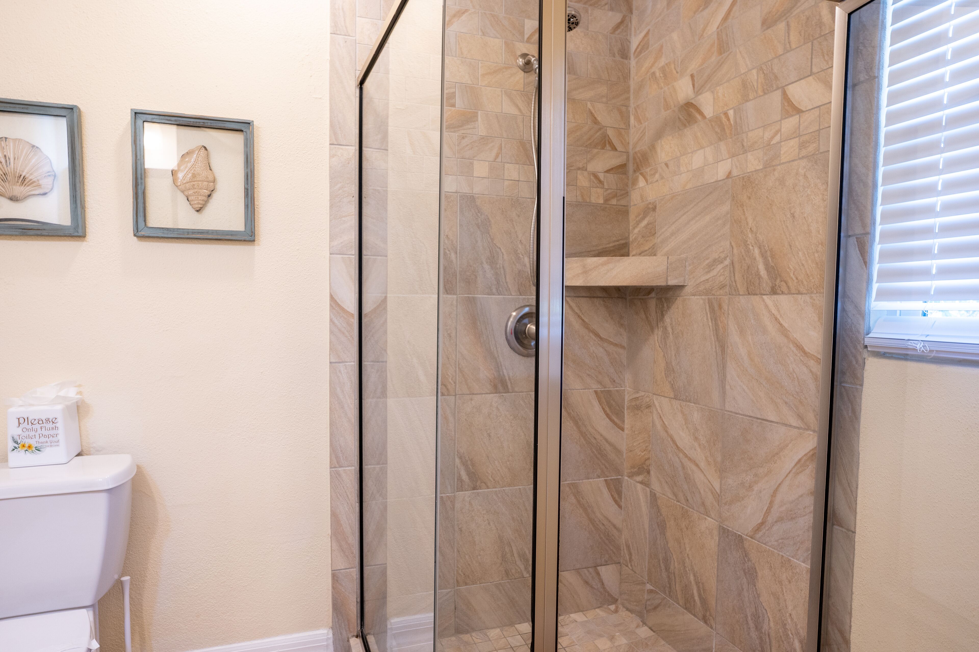 Une salle de bain avec une douche à parois de verre, des murs recouverts de carreaux beiges et des toilettes avec un porte-mouchoirs.
