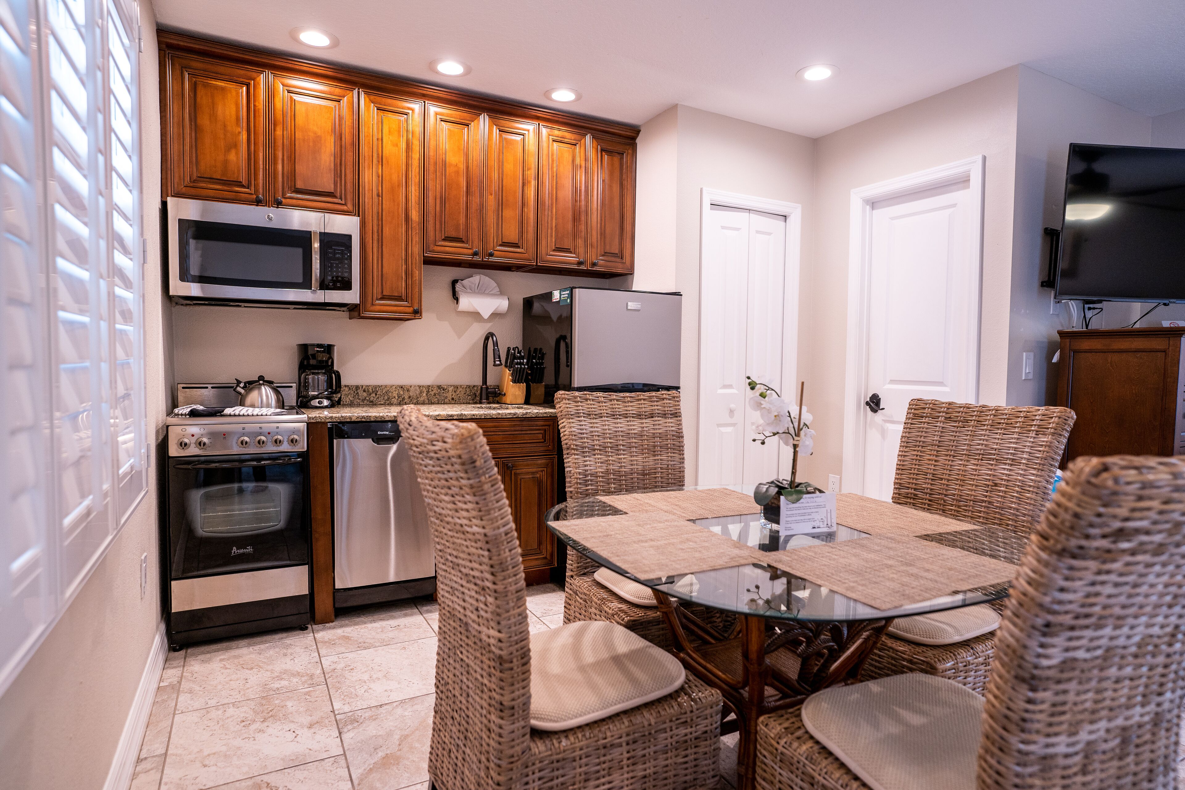 A kitchen with wooden cabinets, stainless steel appliances, wicker chairs, and a glass table.