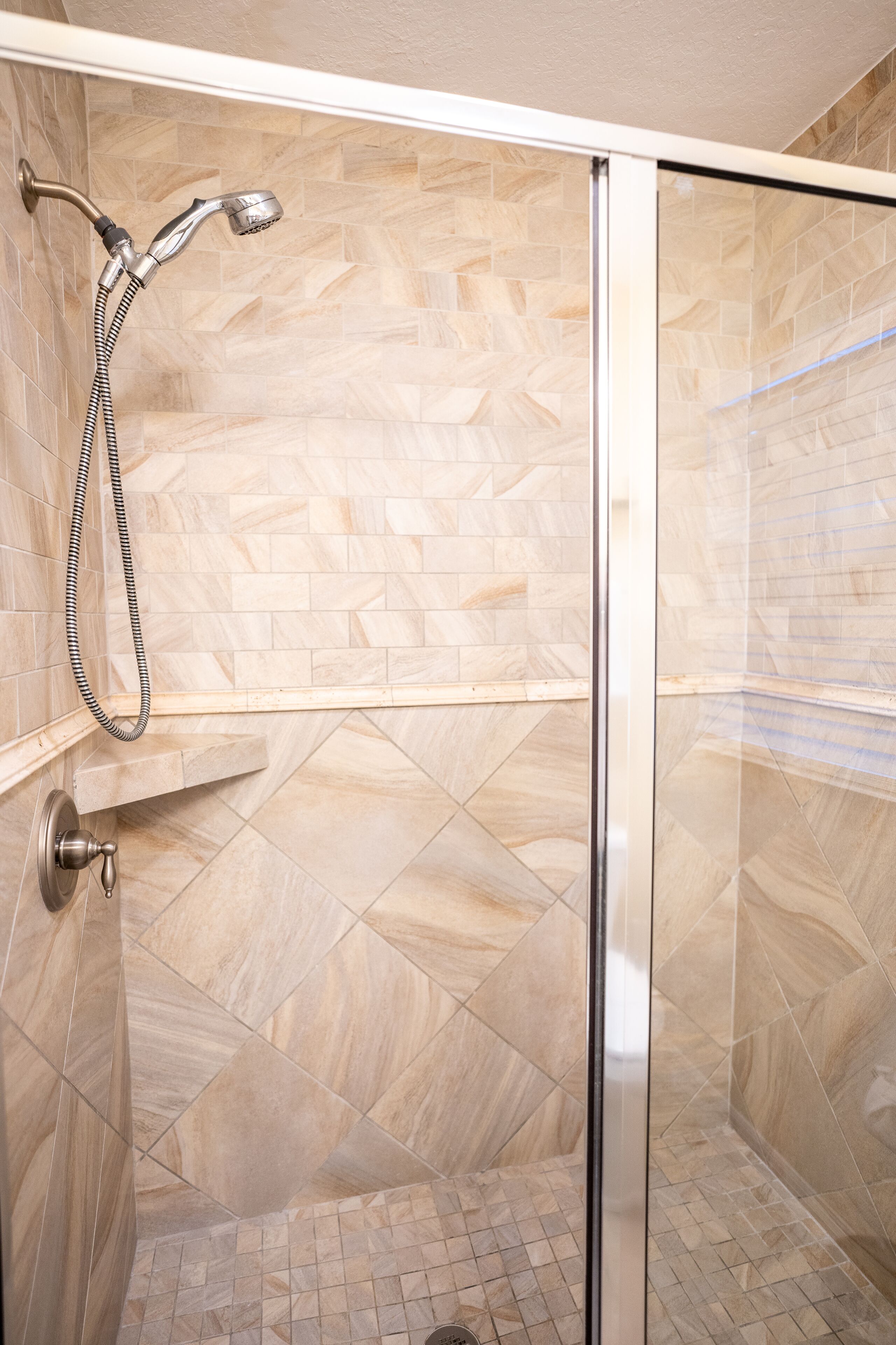 A shower with a glass door, tiled walls, and a showerhead with a hose.