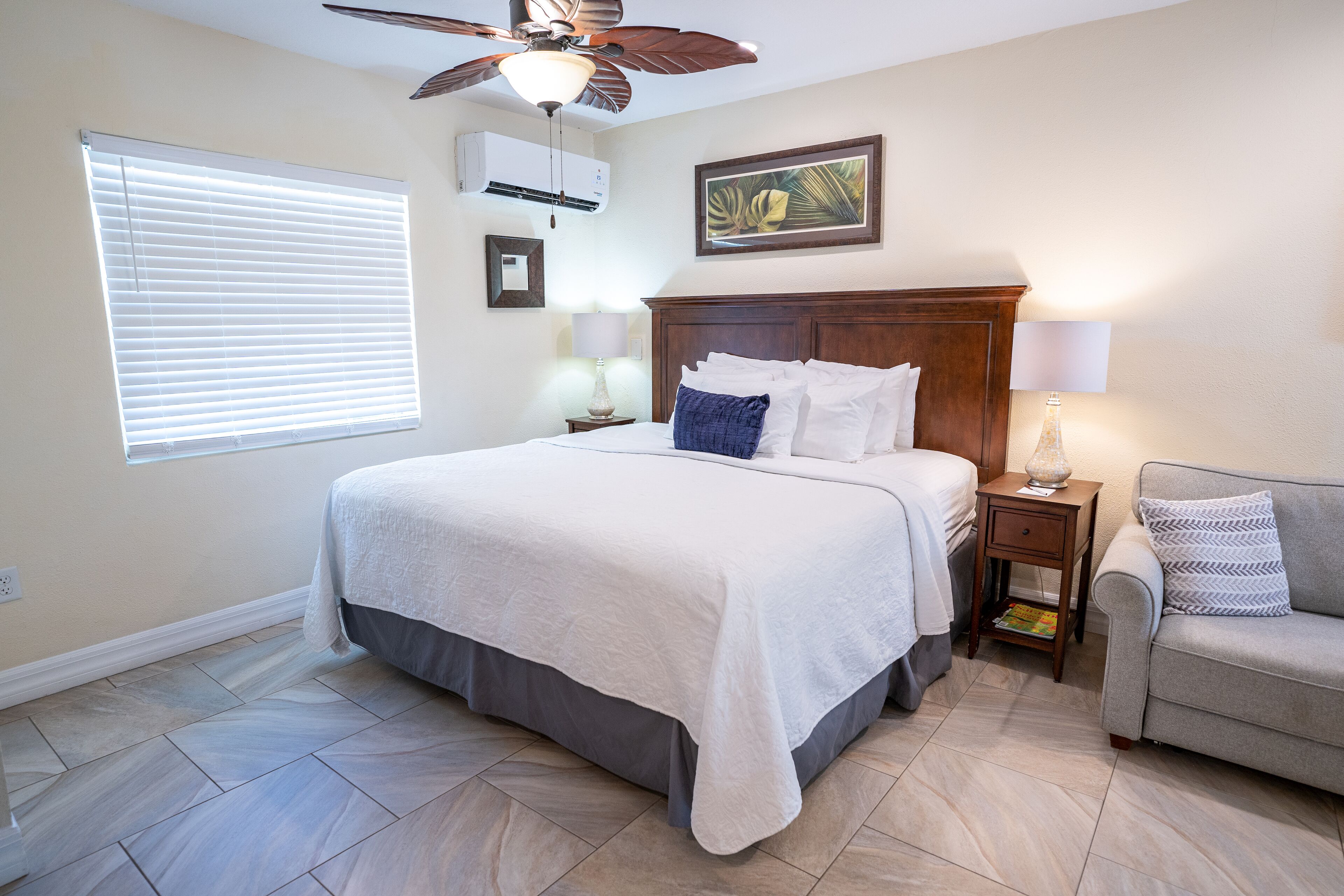 A bedroom with a bed, a nightstand, a lamp, a ceiling fan, and a window with blinds.