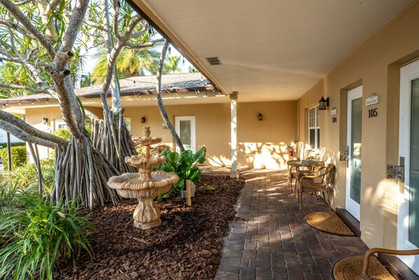 A covered outdoor area with a stone fountain, seating, and a pathway leading to a building entrance.