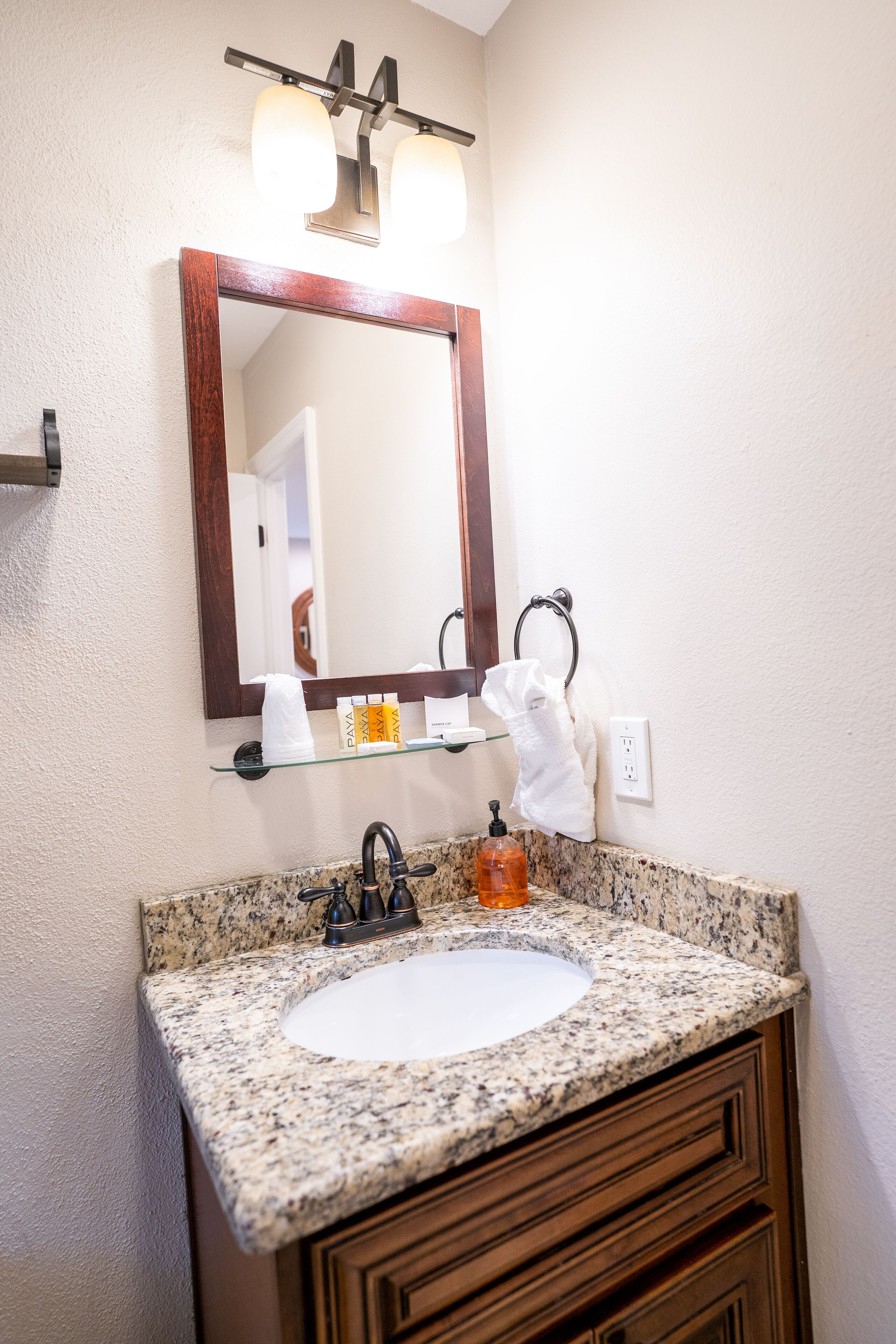 A bathroom with a granite countertop sink, a wooden vanity, a mirror with a wooden frame, and a towel rack.