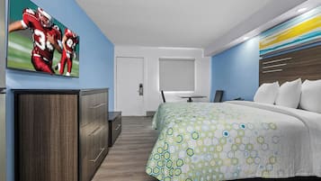 A hotel room with a bed, a desk, a chair, and a television on the wall.
