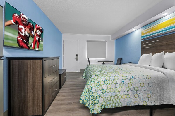 A hotel room with a bed, a desk, a chair, and a television on the wall.