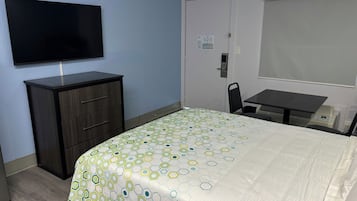 Una habitación de hotel con una cama, un escritorio, una silla, un televisor y un armario.