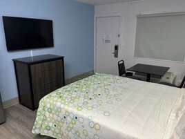 Una habitación de hotel con una cama, un escritorio, una silla, un televisor y un armario.