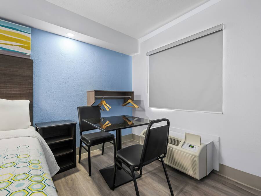 A hotel room with a bed, a desk with a chair, a heater, and a window.