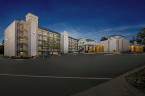 A multi-story hotel with a central entrance, balconies, and a parking lot.