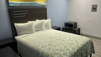 Una habitación de hotel con cama, mesita de noche, televisor montado en la pared y un cuadro sobre la cama.