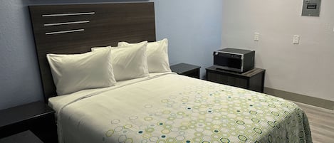 A hotel room with a bed, a nightstand, a wall-mounted TV, and a painting above the bed.