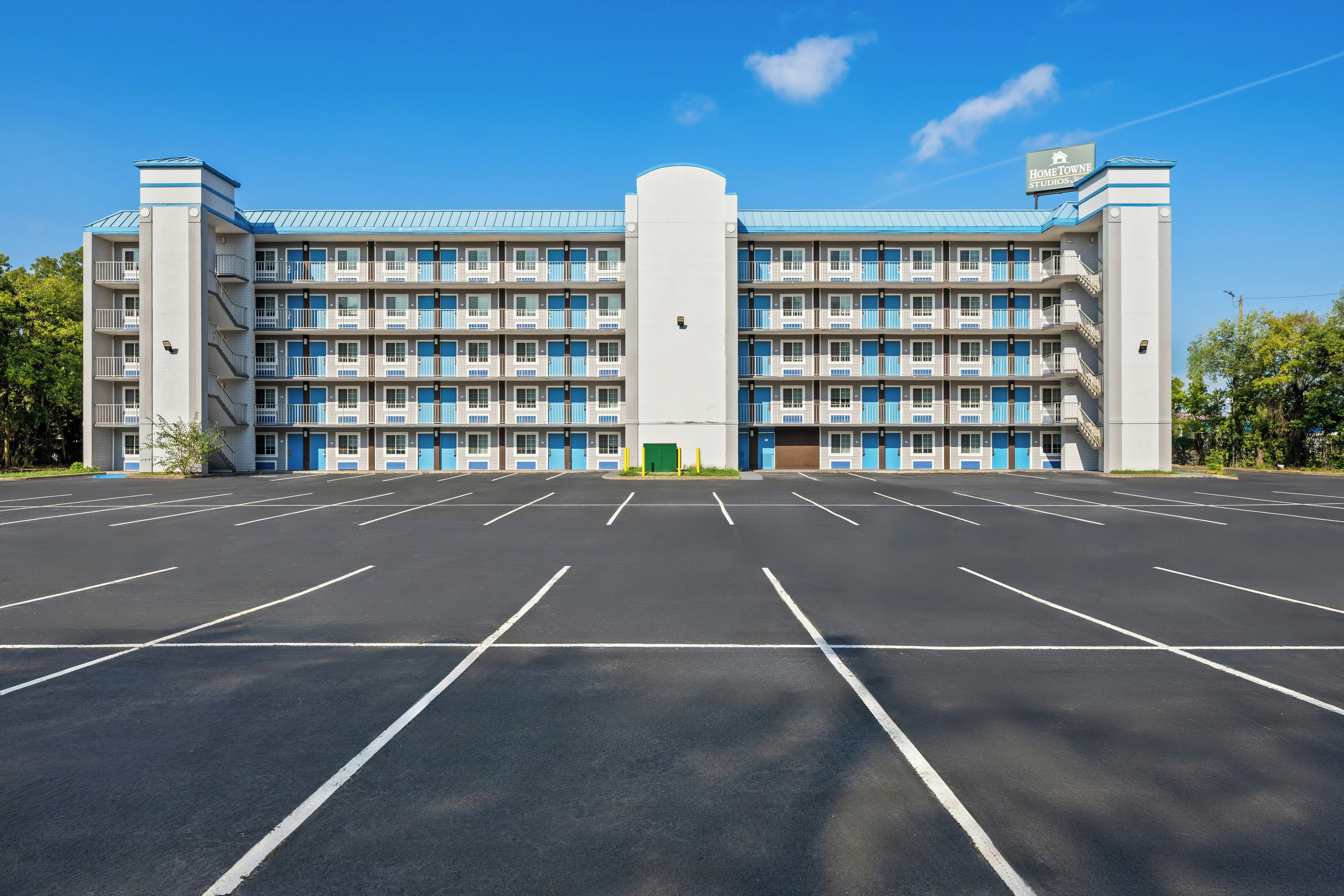 Un hotel de varios pisos con una entrada central y un estacionamiento frente a él.