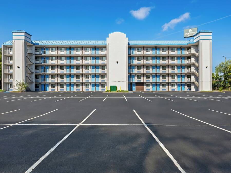 A multi-story hotel with a central entrance and a parking lot in front.