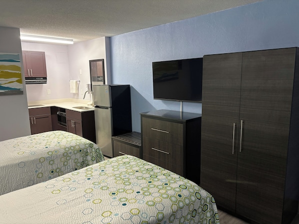A hotel room with two beds, a kitchenette, a television, and a wardrobe.