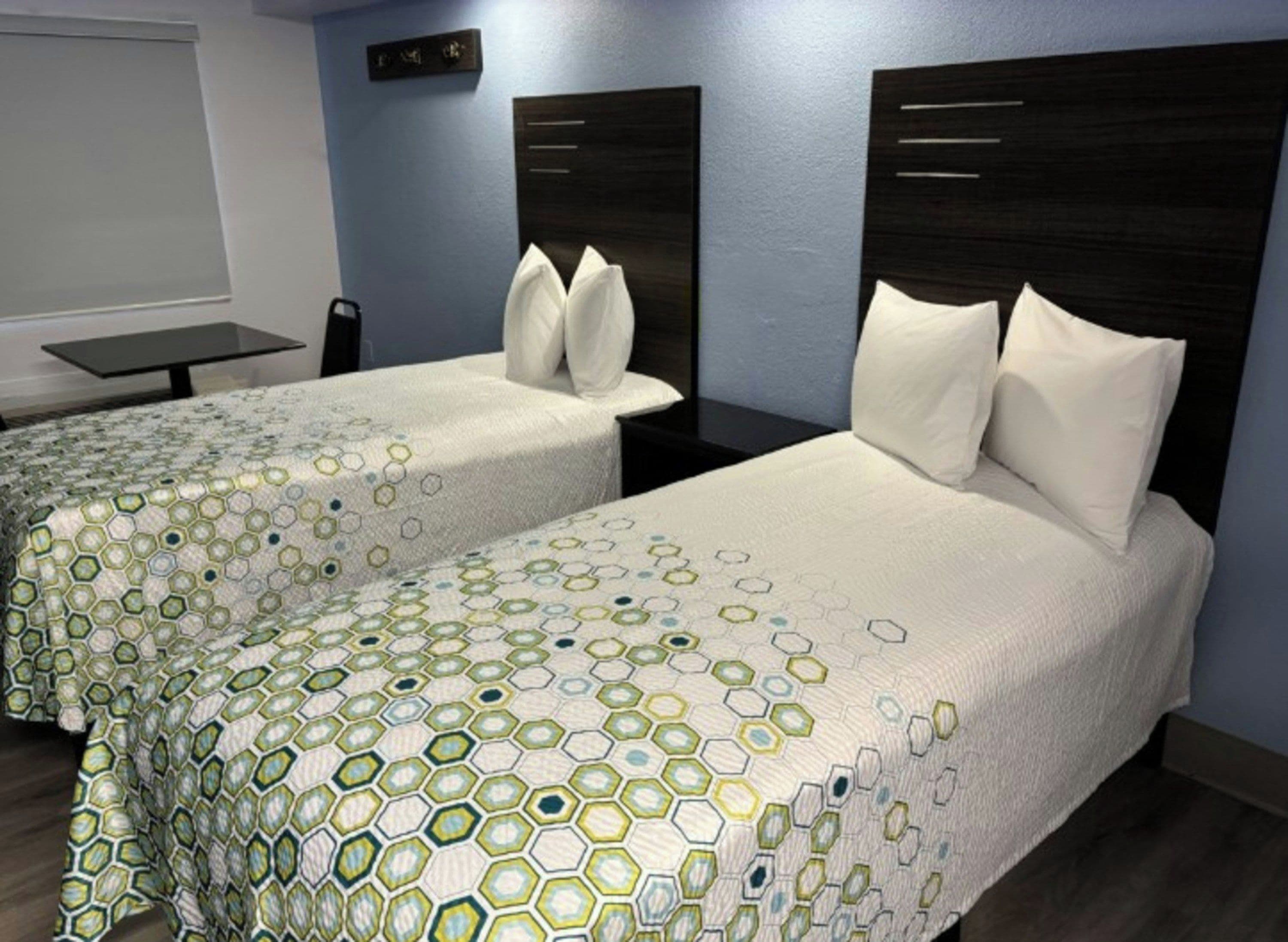 Two twin beds with a geometric patterned bedspread, a dark headboard, and a small table with a chair.