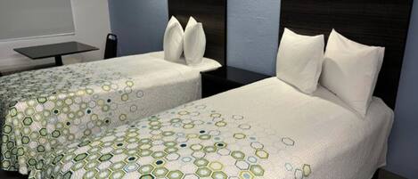 Two twin beds with a geometric patterned bedspread, a dark headboard, and a small table with a chair.