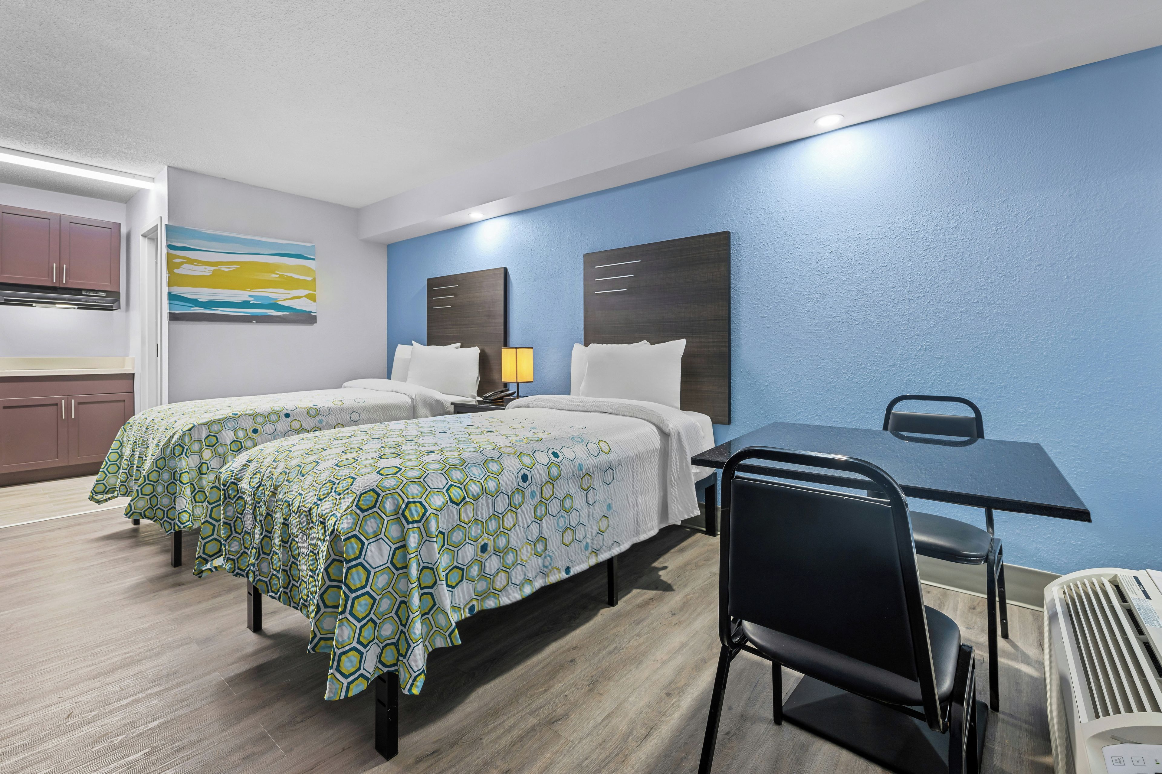 Une chambre d’hôtel avec deux lits, un bureau, une chaise et une kitchenette.