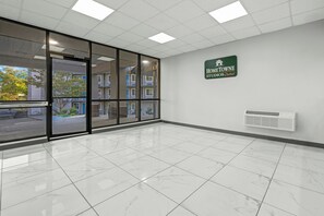 A clean, modern interior with a glass door entrance, a sign for 'Home Towe Studios by Red Roof', and a white air conditioning unit on the wall. - HomeTowne Studios by Red Roof Birmingham - Airport (Birmingham)