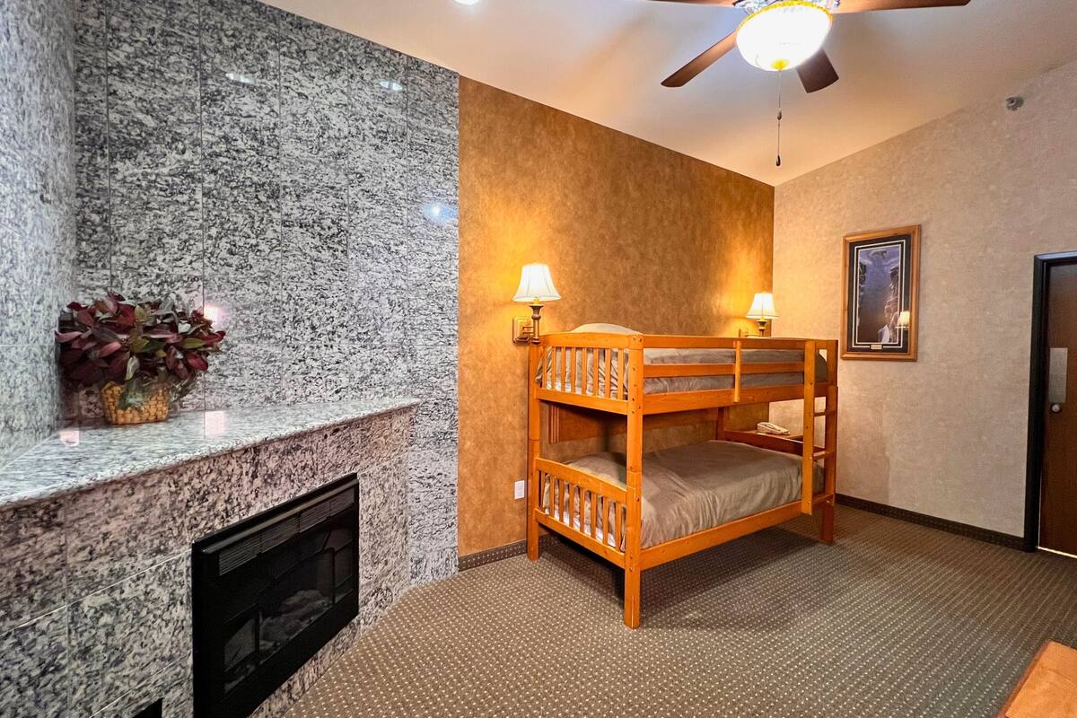A room with a bunk bed, a fireplace, a ceiling fan, and a framed picture on the wall.