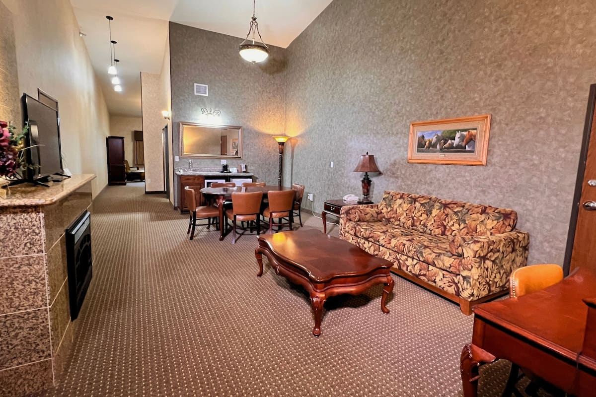 A hotel room with a dining area, a sofa, a wooden coffee table, and a TV on a stand.