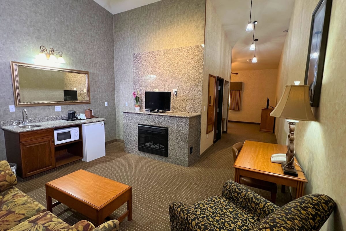 A compact hotel room with a kitchenette, a fireplace, a TV, a sofa, and a small dining table.