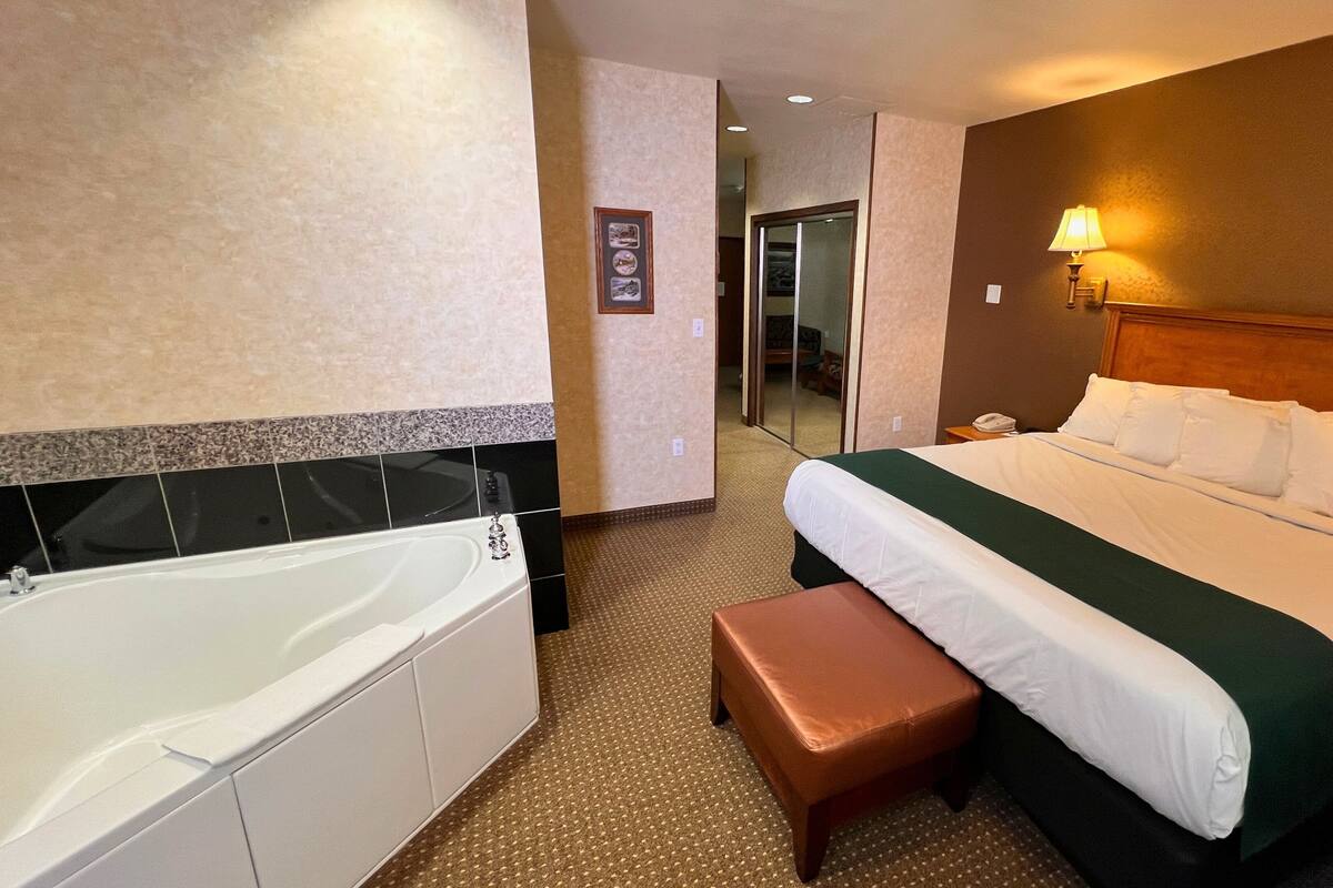 A hotel room with a large bed, a separate bathroom with a bathtub, and a small sitting area.