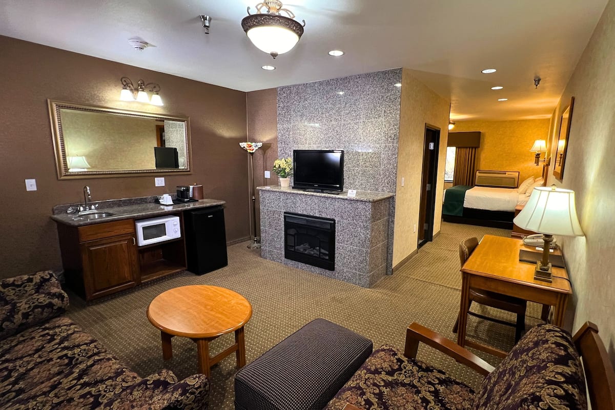 A hotel room with a living area, kitchenette, fireplace, and a separate bedroom.