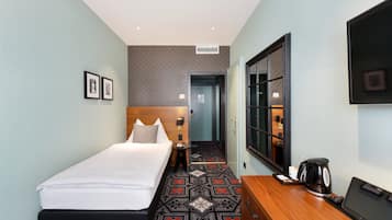 A hotel room with a bed, a desk with a coffee maker, a TV, and a picture frame on the wall.