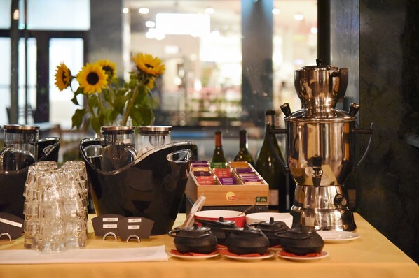 Una estación de café con diferentes equipos de preparación y cápsulas de café, una variedad de vasos y un jarrón con girasoles.