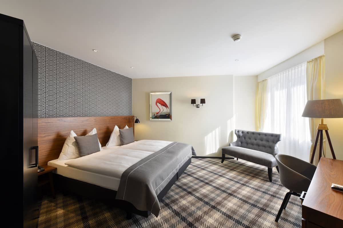 Habitación de hotel con una cama grande, un escritorio, una silla, una lámpara y un cuadro en la pared.