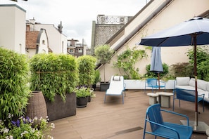 Une terrasse sur le toit, aménagée avec des espaces de détente en plein air, des plantes en pot et offrant une vue sur le paysage urbain.