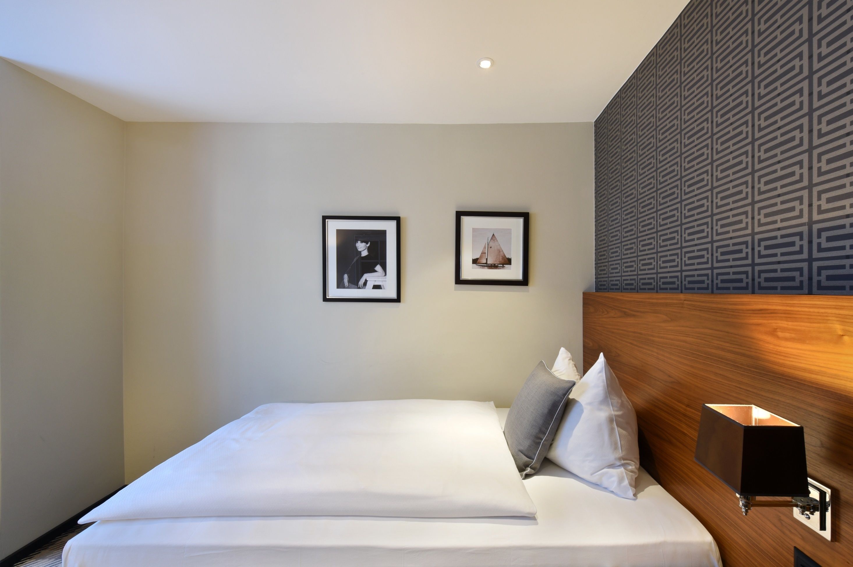 Una habitación de hotel con una cama bien hecha, dos cuadros enmarcados en la pared y un cabecero moderno con un diseño geométrico.