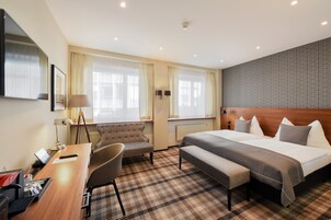 Una habitación de hotel con una cama grande, un escritorio con silla, un sofá y una ventana con cortinas.