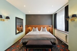 Une chambre d’hôtel avec un grand lit, une tête de lit en bois, une fenêtre avec des rideaux et un sol à motifs.
