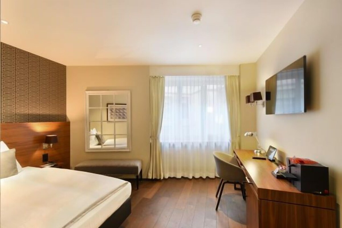 Habitación de hotel con cama, escritorio, silla y televisión en la pared.