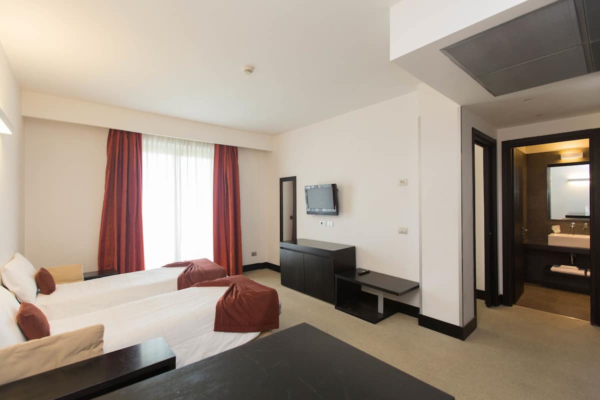 A hotel room with two beds, a desk, a television, and a bathroom with a mirror and sink.