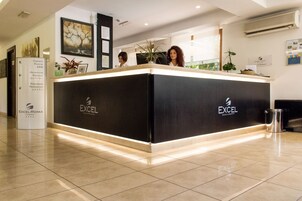 Una recepción de hotel con un mostrador negro y bordes iluminados, un cartel con indicaciones de las habitaciones y una obra de arte enmarcada en la pared.