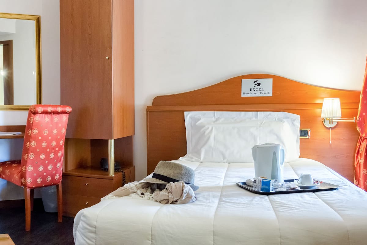 A hotel room with a bed, a desk, a chair, a mirror, and a sign indicating the hotel name.