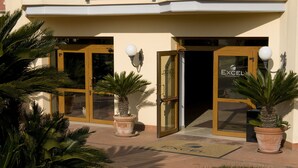 Entrada d'hotel amb portes de vidre, una palmera i un felpó amb el nom de l'hotel.