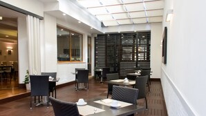 Zona d'esmorzar interior i moderna, amb terres de fusta, cadires de vímet negre i taules preparades amb gots i plats blancs.