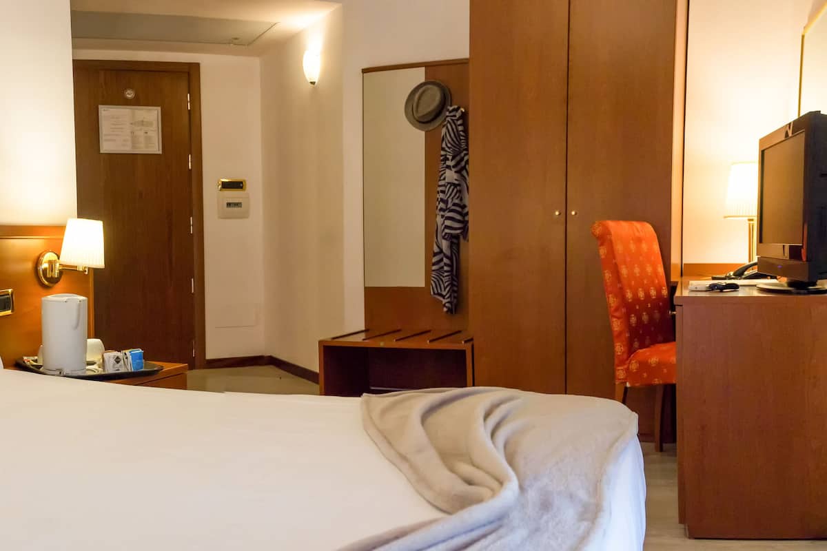 A hotel room with a large bed, a desk with a computer, a chair, and a lamp.