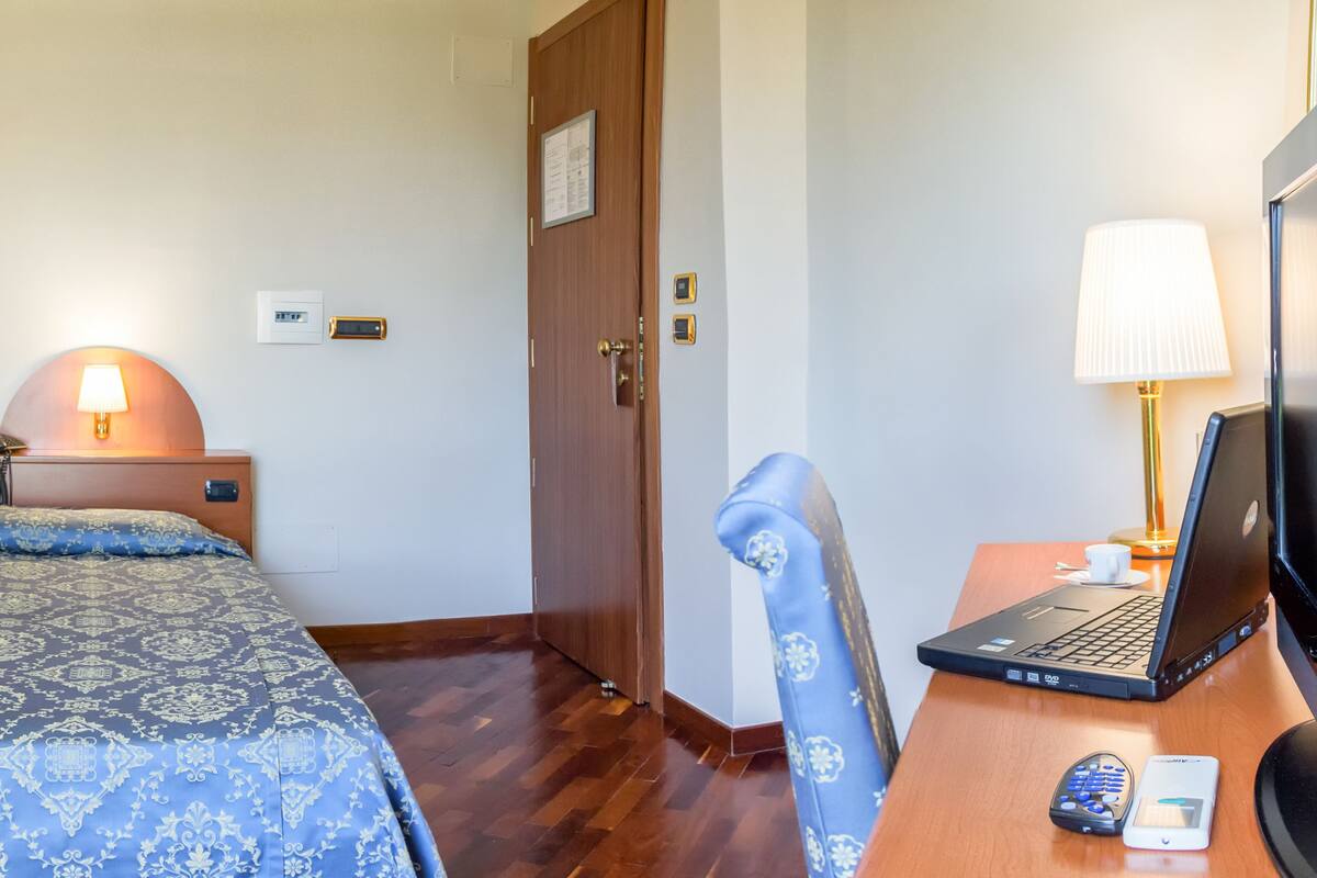 A hotel room with a shower, a bed with a patterned bedspread, a desk with a laptop, and a chair.